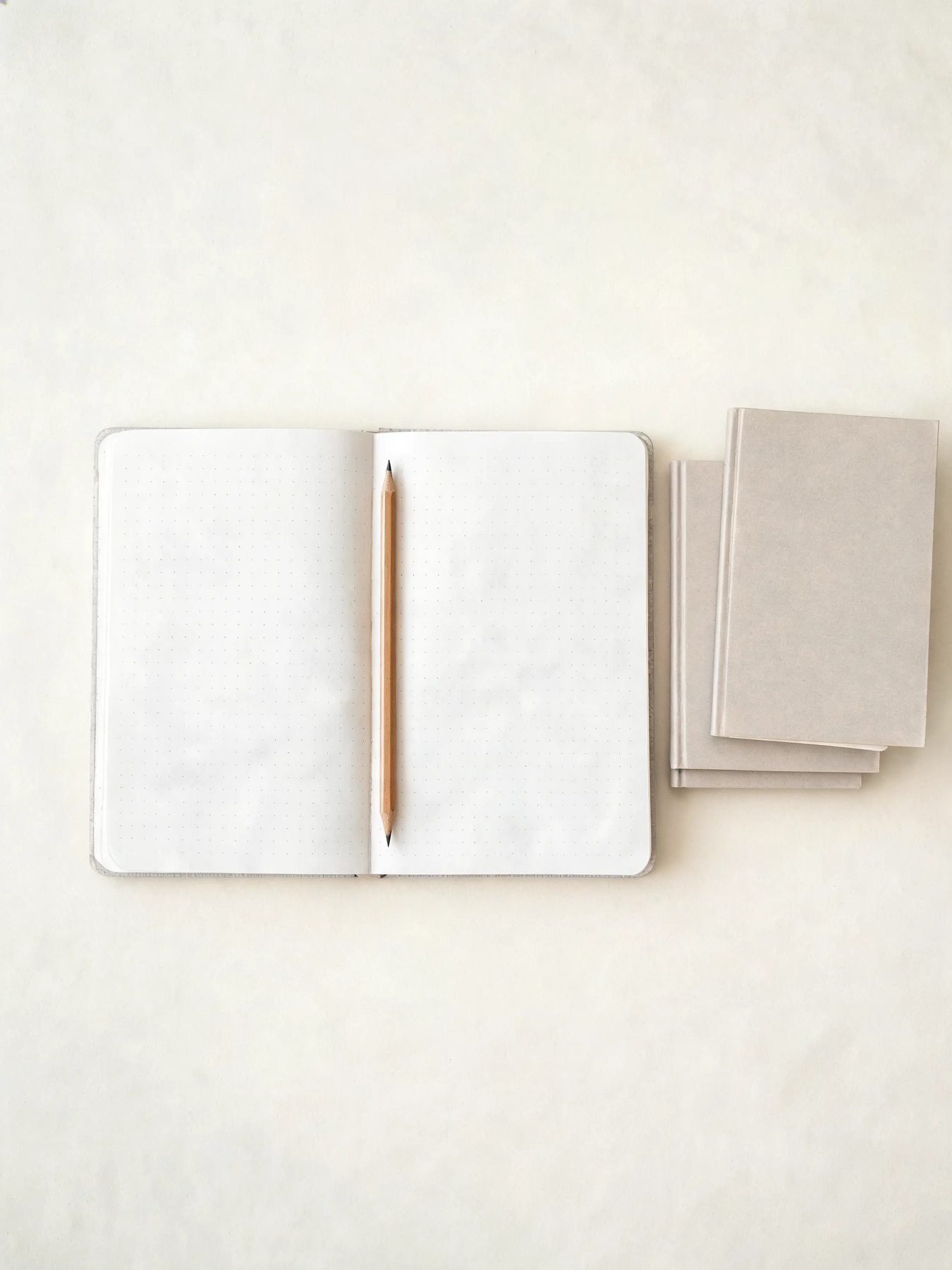 Open dotted notebook with a graphite pencil and two pocket books stacked beside it